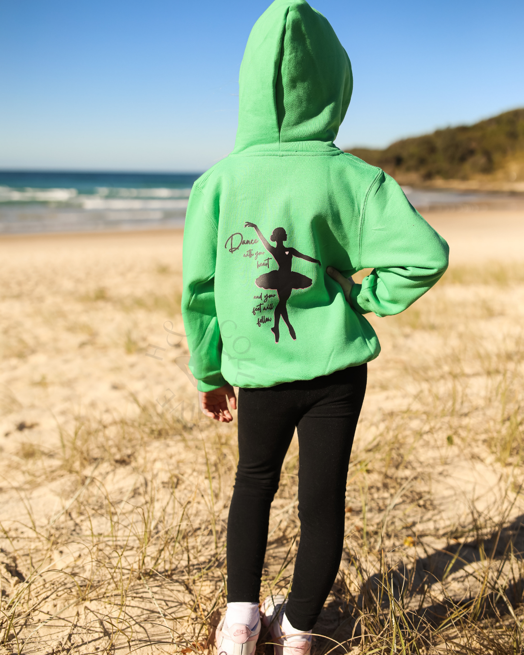 Person wearing a green hoodie with a black silhouette design on a beach