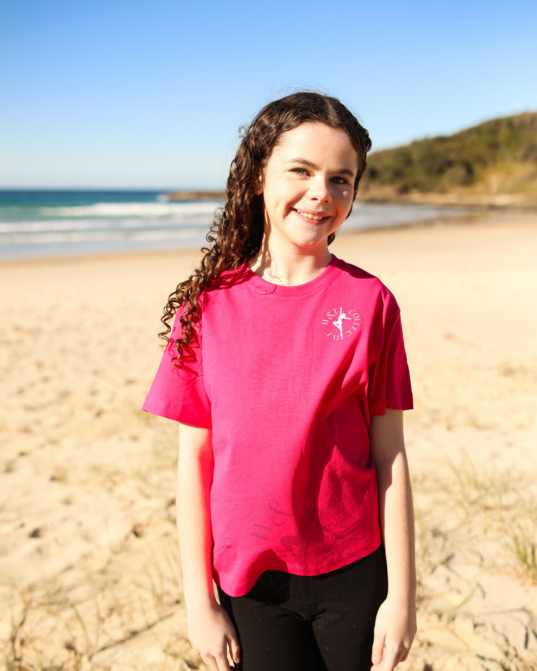 Person wearing a pink t-shirt on a beach with ocean and sky in the background