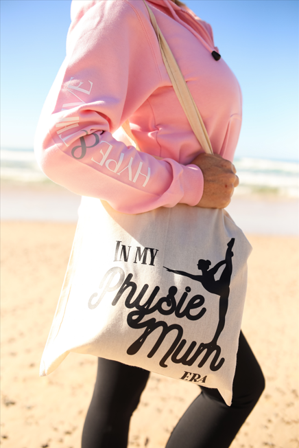 Person wearing a pink jacket and carrying a tote bag with text on a beach.
