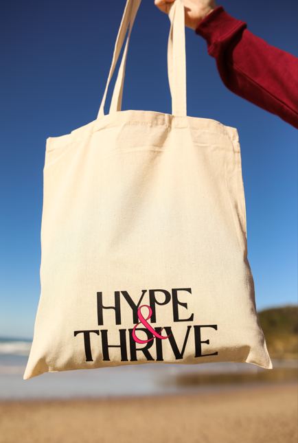 Tote bag with 'Hype & Thrive' text held by a person on a beach