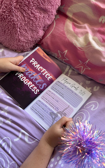 Person holding a book titled 'Practice Makes Progress' on a bed with pink pillows and a purple blanket.