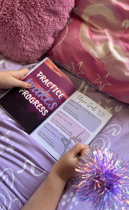 Person holding a book titled 'Practice Makes Progress' on a bed with pink pillows and a purple blanket.